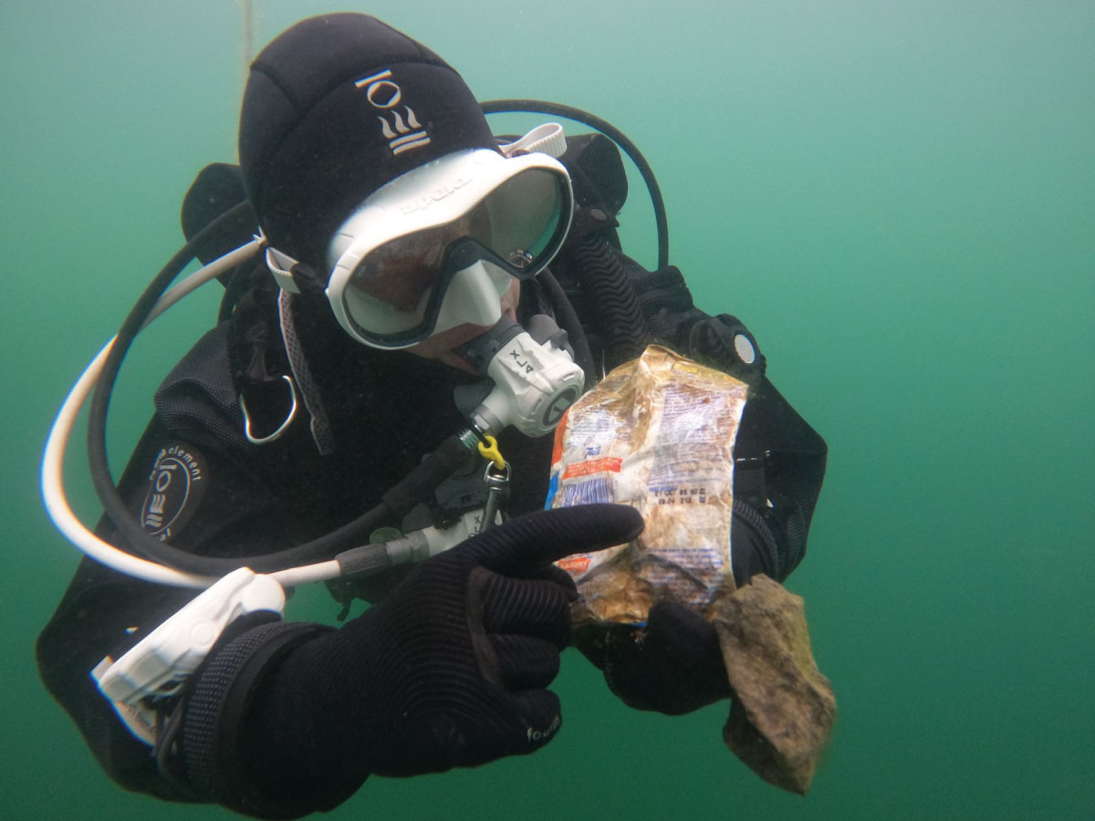 Diver holding an old crisp packet underwater, highlighting the importance of buoyancy in eco-diving