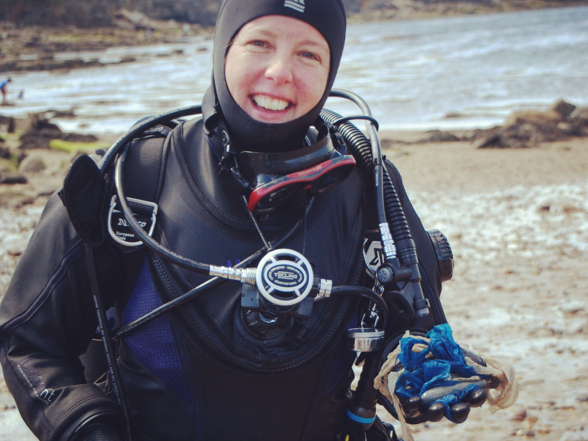 Smiling diver walking out of the ocean holding trash, practicing eco-diving